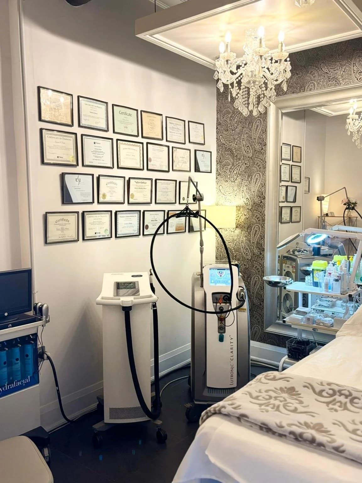 Exsalonce treatment room with chandelier, laser equipment, and certificate wall